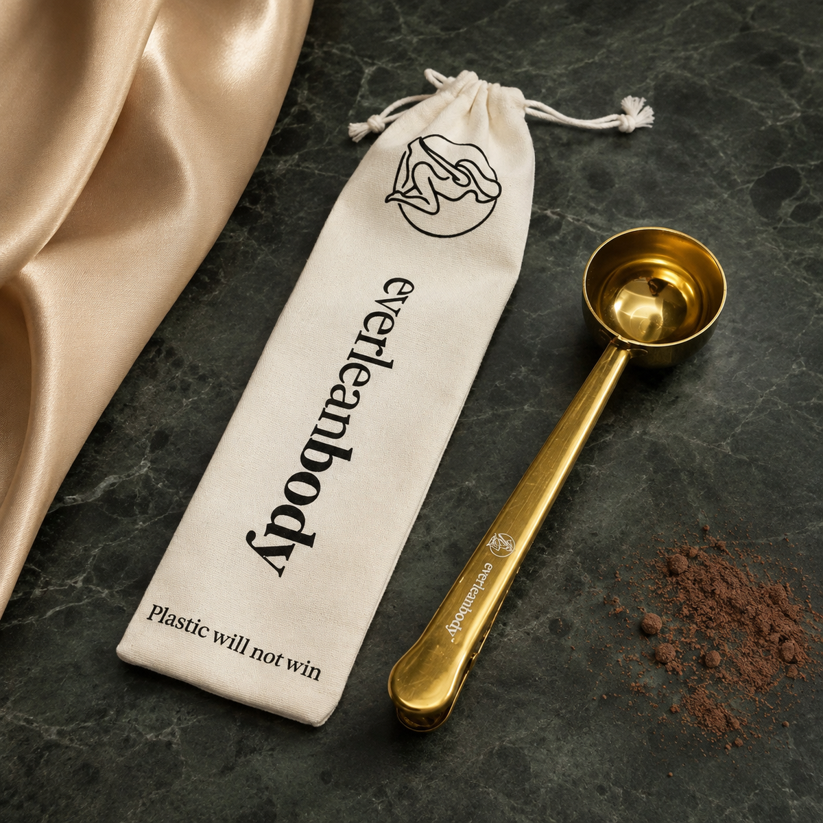 EverLeanBody gold stainless steel scoop with engraved logo, next to its cotton drawstring bag printed with Plastic will not win